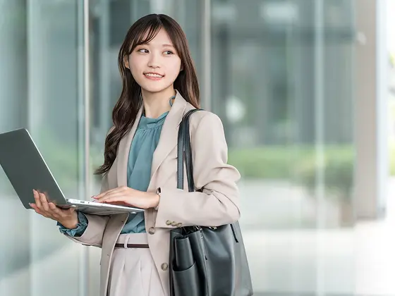 写真：スーツ姿の女性がパソコンを持っています。